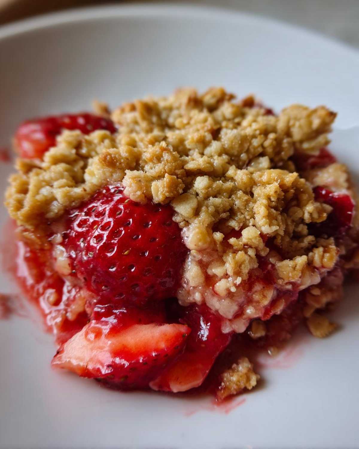 A close-up serving of warm Strawberry Rhubarb Crisp showing juicy strawberries and a golden crumble topping.