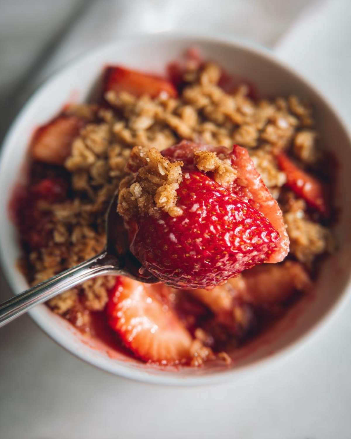 A spoonful of warm Strawberry Rhubarb Crisp featuring a large, juicy strawberry piece and oat topping.