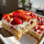 A close-up shot of a moist slice of Strawberry Shortcake Sheet Cake being lifted with a server, topped with whipped cream and fresh strawberries.
