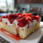 A close-up of a moist slice of Strawberry Shortcake Sheet Cake topped with whipped cream and glazed strawberries.