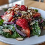 Close-up of a vibrant Strawberry Spinach Salad with poppy seed dressing, sliced strawberries, red onion, and toasted almonds.