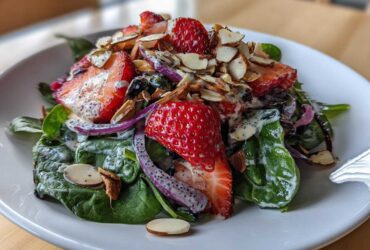 Close-up of a vibrant Strawberry Spinach Salad with poppy seed dressing, sliced strawberries, red onion, and toasted almonds.