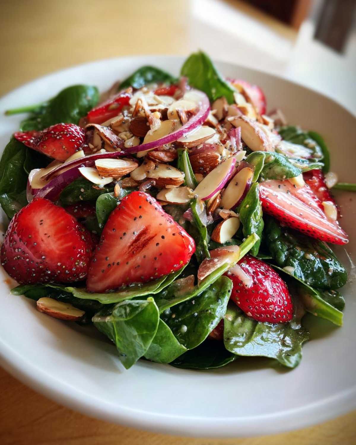 Close-up of a vibrant Strawberry Spinach Salad with poppy seed dressing, sliced strawberries, almonds, and red onion.