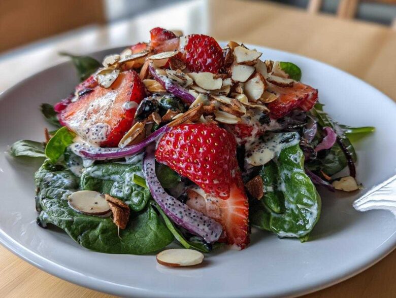 Close-up of a vibrant Strawberry Spinach Salad with poppy seed dressing, sliced strawberries, red onion, and toasted almonds.
