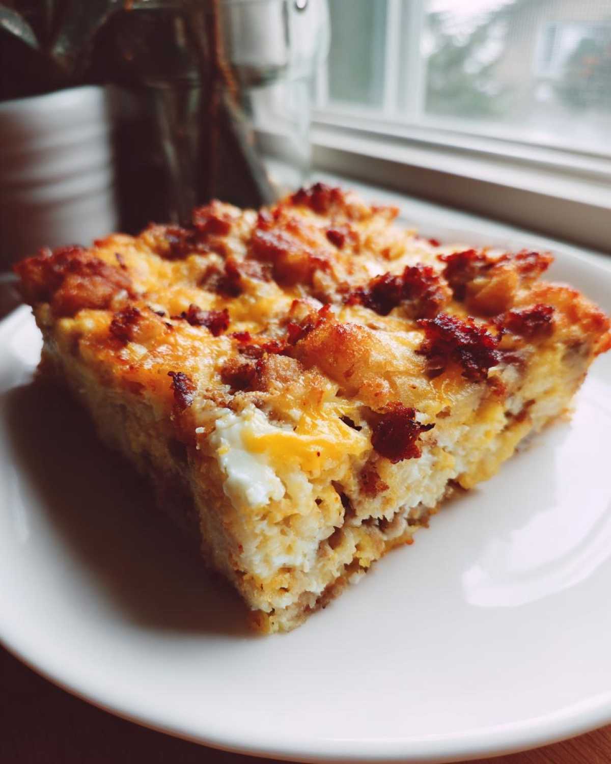 A close-up slice of Tater Tot Breakfast Casserole featuring eggs, cheese, and sausage crumbles on a white plate.