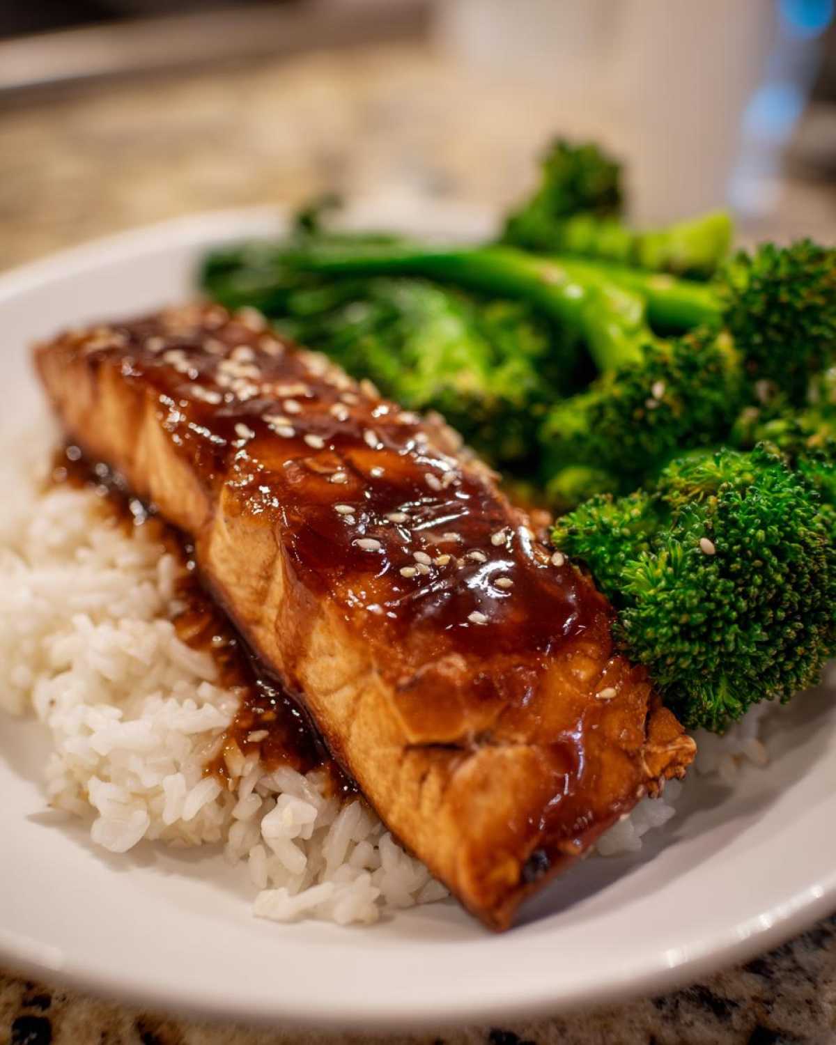 Close-up of a perfectly cooked salmon fillet glazed with teriyaki sauce and sesame seeds served over white rice with steamed broccoli, part of Teriyaki Salmon Rice Bowls.
