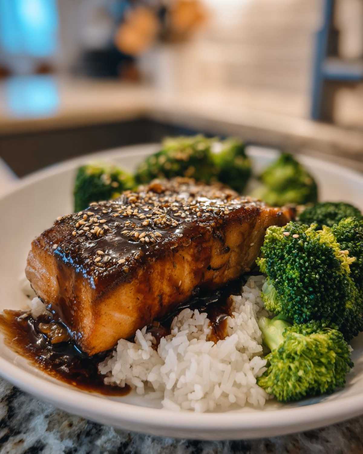 Close-up of a perfectly cooked salmon fillet glazed with teriyaki sauce and sesame seeds over white rice and broccoli.