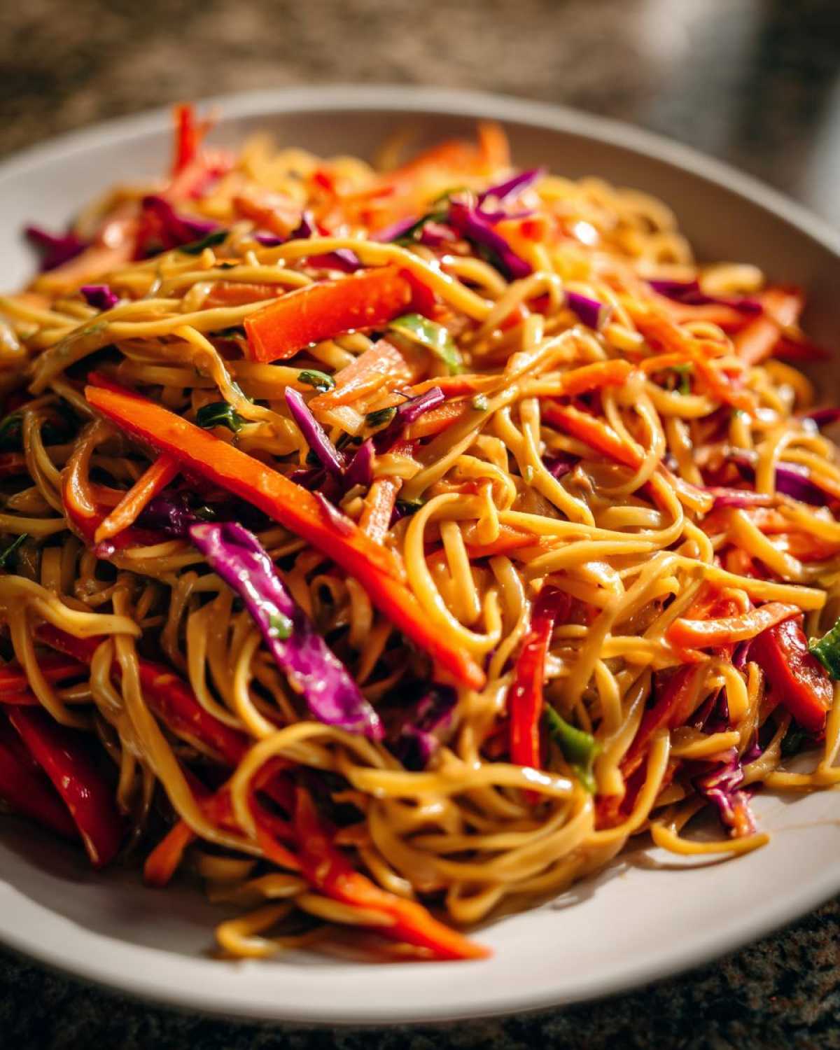 A close-up shot of a bowl filled with saucy Thai Peanut Noodles with Crunchy Veggies, featuring bright red peppers and purple cabbage.