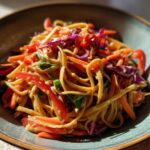 Close-up of a bowl of Thai Peanut Noodles with Crunchy Veggies, featuring noodles coated in peanut sauce and mixed with bright red peppers and carrots.