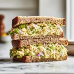 A tall stack of two halves of a Vegan Chickpea Salad Sandwich made with whole wheat bread and creamy filling.