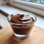 A close-up of rich, dark Vegan Chocolate Avocado Mousse swirled high in a small clear glass cup.