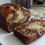 Close-up of a freshly baked Vegan Chocolate Banana Bread loaf with one slice cut, showing gooey melted chocolate chips inside.