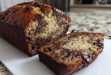 Close-up of a freshly baked Vegan Chocolate Banana Bread loaf with one slice cut, showing gooey melted chocolate chips inside.