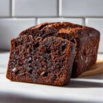 A close-up of moist Vegan Chocolate Banana Bread, showing a slice cut from the loaf filled with melted chocolate chips.