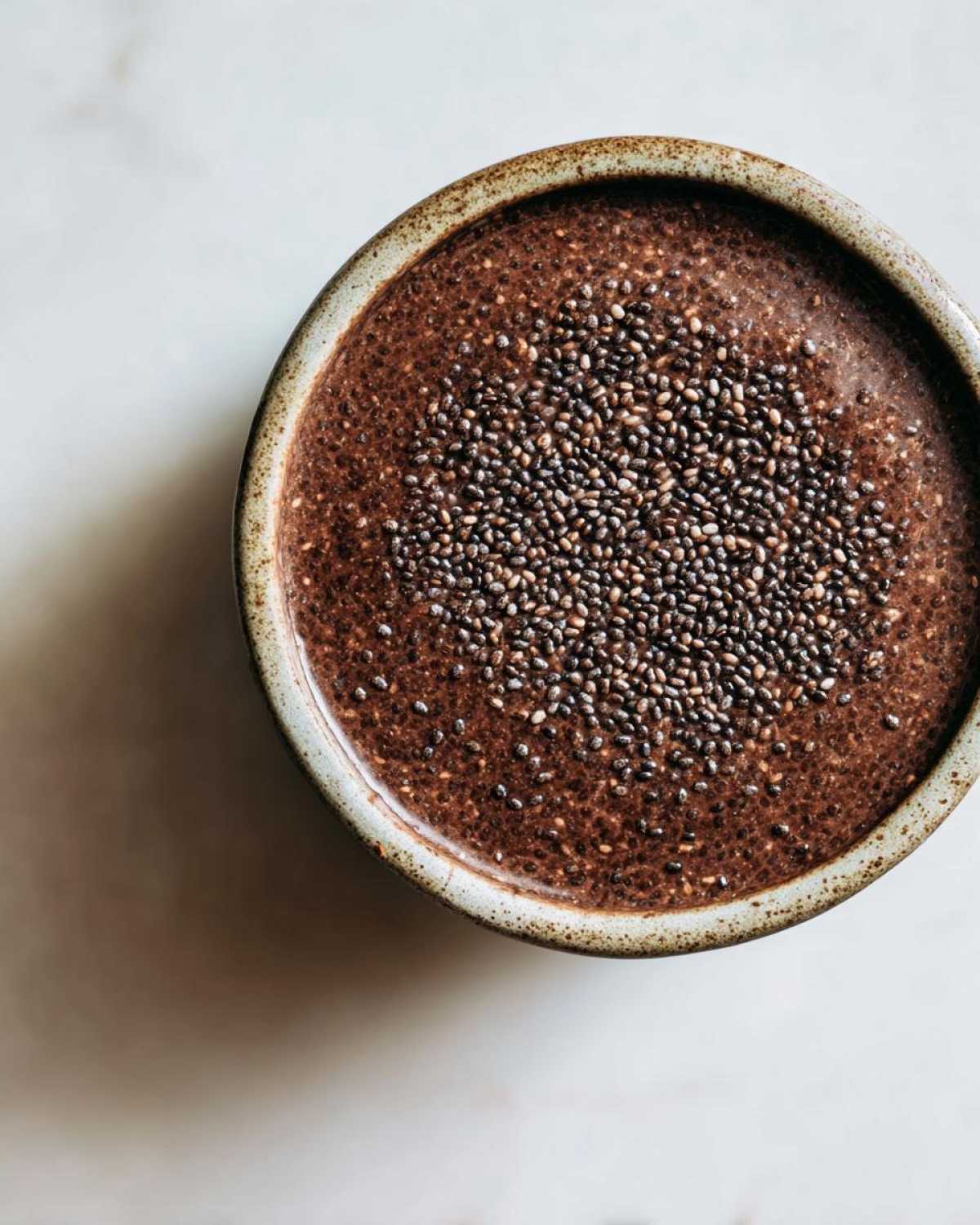 Overhead view of rich Vegan Chocolate Chia Pudding topped generously with whole chia seeds in a rustic bowl.