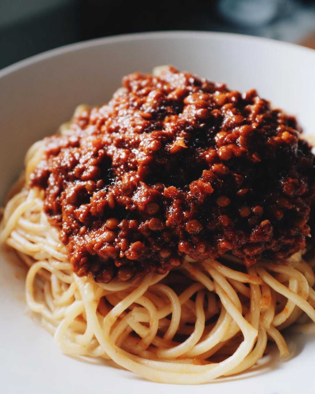 Close-up of a white bowl filled with spaghetti topped generously with rich Vegan Lentil Bolognese sauce.