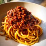 Close-up of a hearty serving of Vegan Lentil Bolognese piled high on spaghetti noodles in a white bowl.