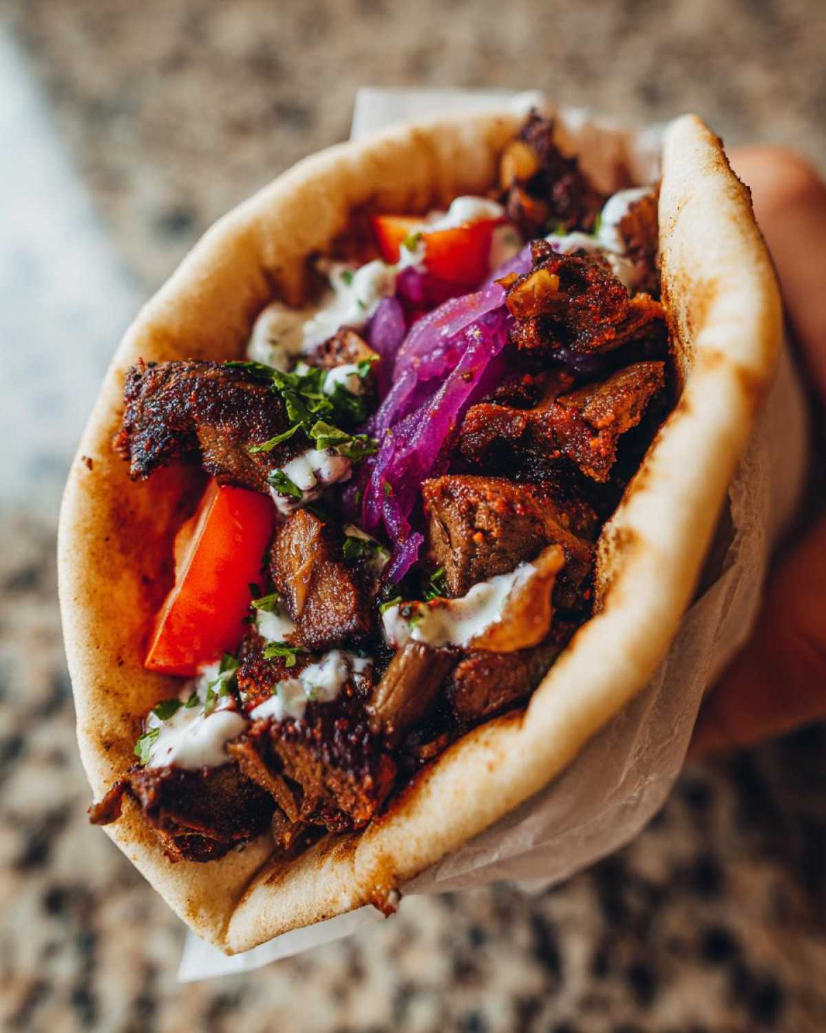 Close-up of a handheld Vegan Mushroom Shawarma stuffed with seasoned mushrooms, pickled onions, tomatoes, and white sauce