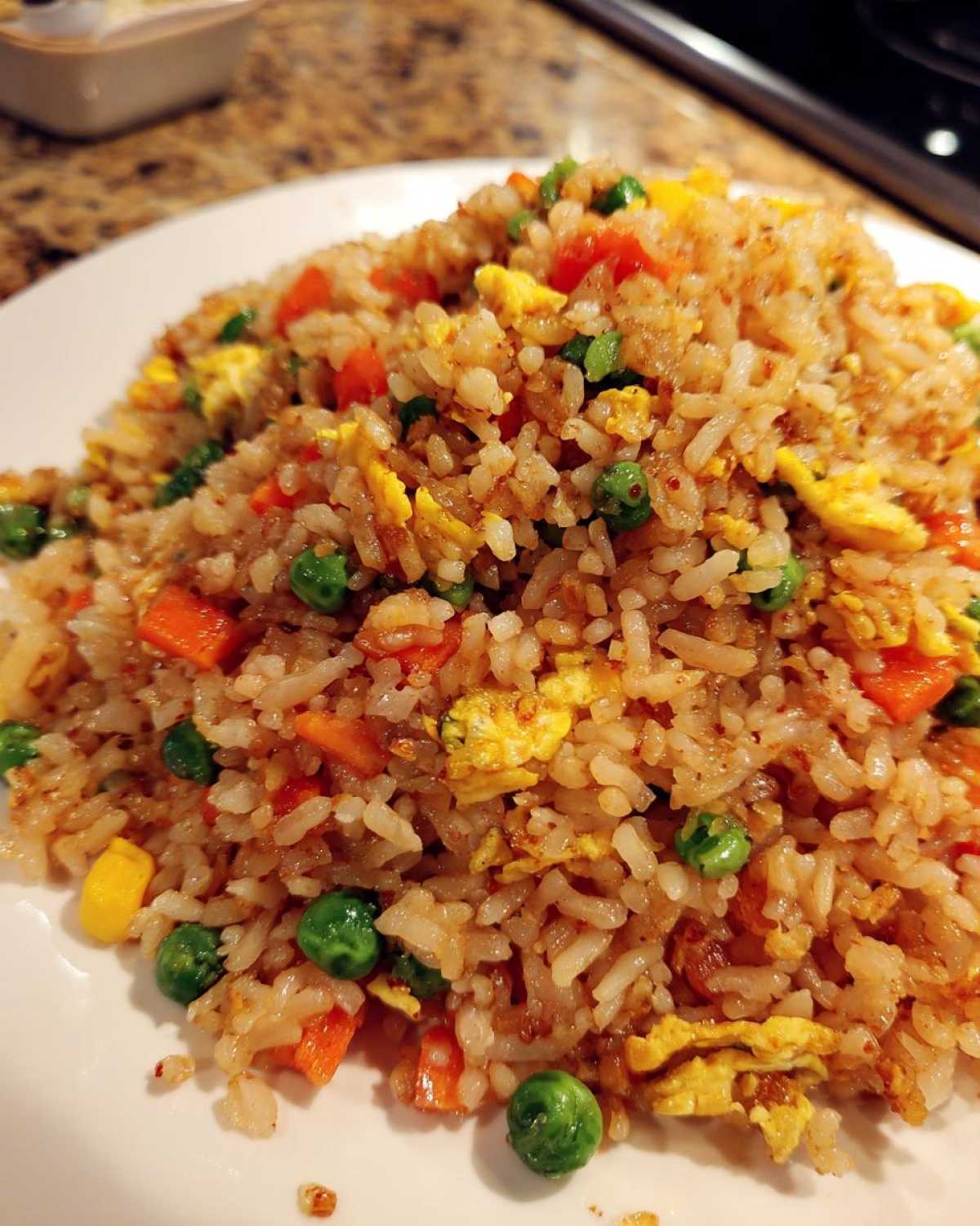 A close-up image of freshly made Vegetable Fried Rice with visible pieces of scrambled egg, carrots, and green peas.