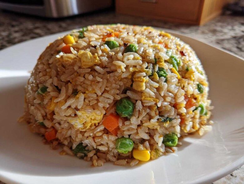 A perfectly molded dome of Vegetable Fried Rice with mixed peas, carrots, corn, and scrambled egg on a white plate.
