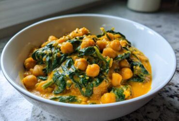 Close-up of a white bowl filled with rich, creamy Vegetarian Chickpea Curry with Coconut Milk and wilted spinach.