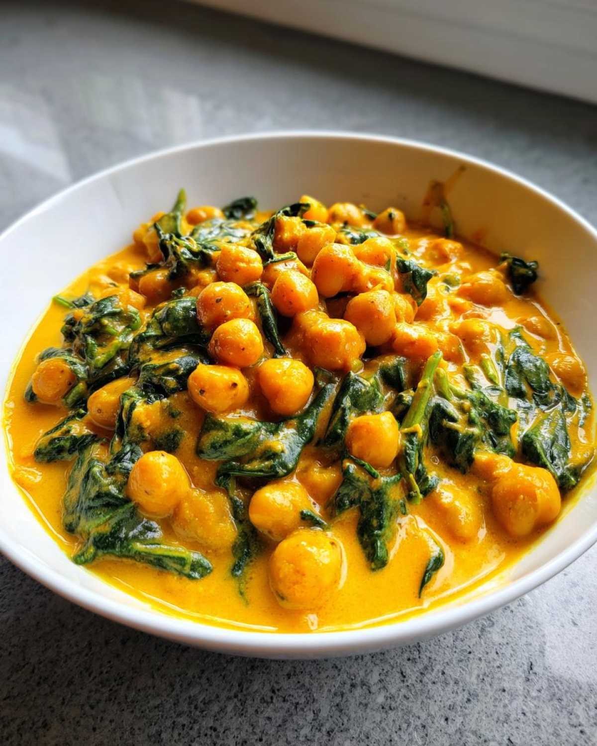 A bowl of vibrant yellow Vegetarian Chickpea Curry with coconut milk and wilted spinach.
