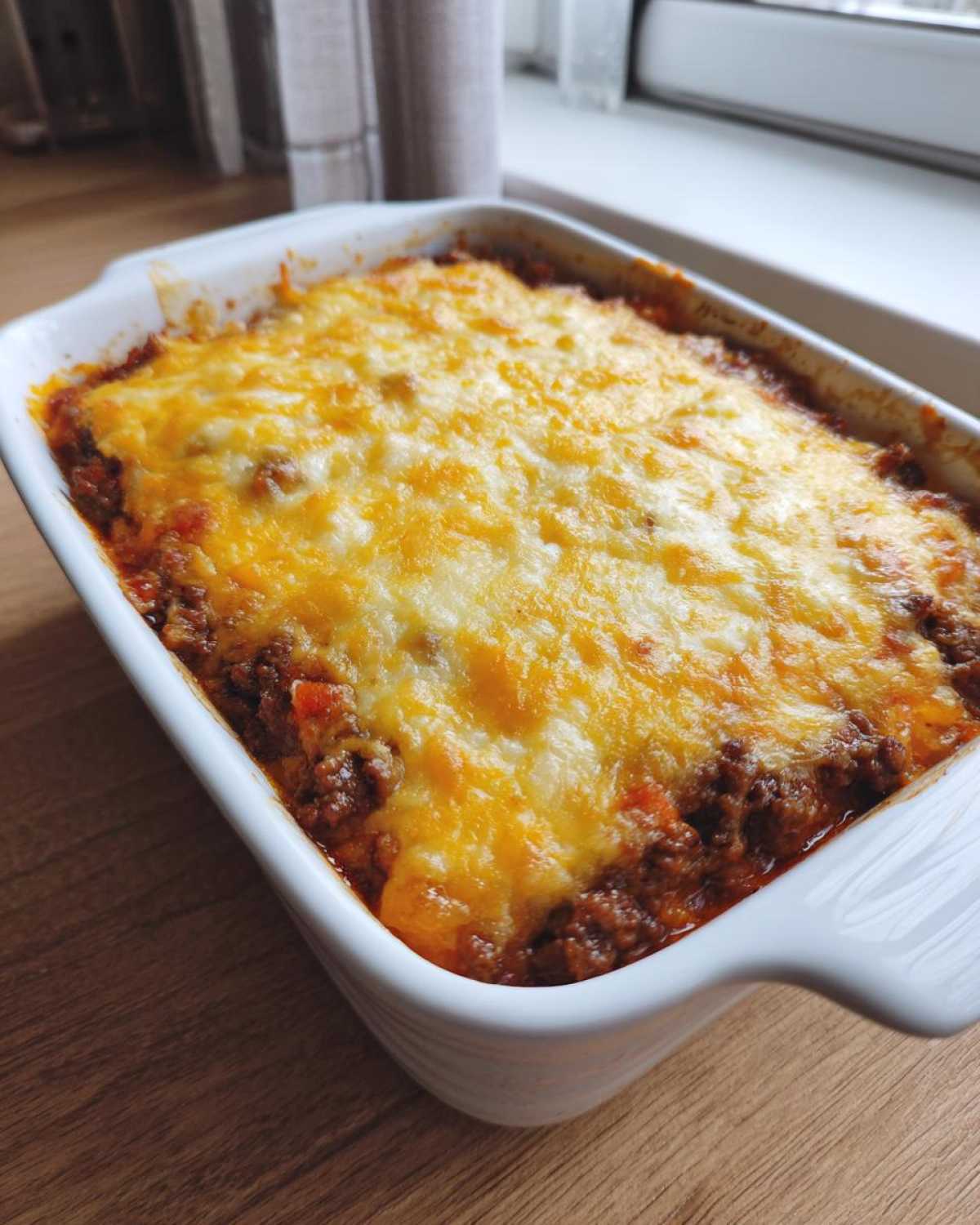 A white baking dish filled with hot Cheesy Beef and Rice Casserole, topped with melted golden cheese.