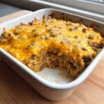 A close-up of a baked Cheesy Beef and Rice Casserole Comfort Dish topped with melted cheddar cheese in a white square baking dish.