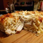 A slice of Cheesy Chicken Alfredo Bake showing melted cheese stretching between the chicken and pasta.