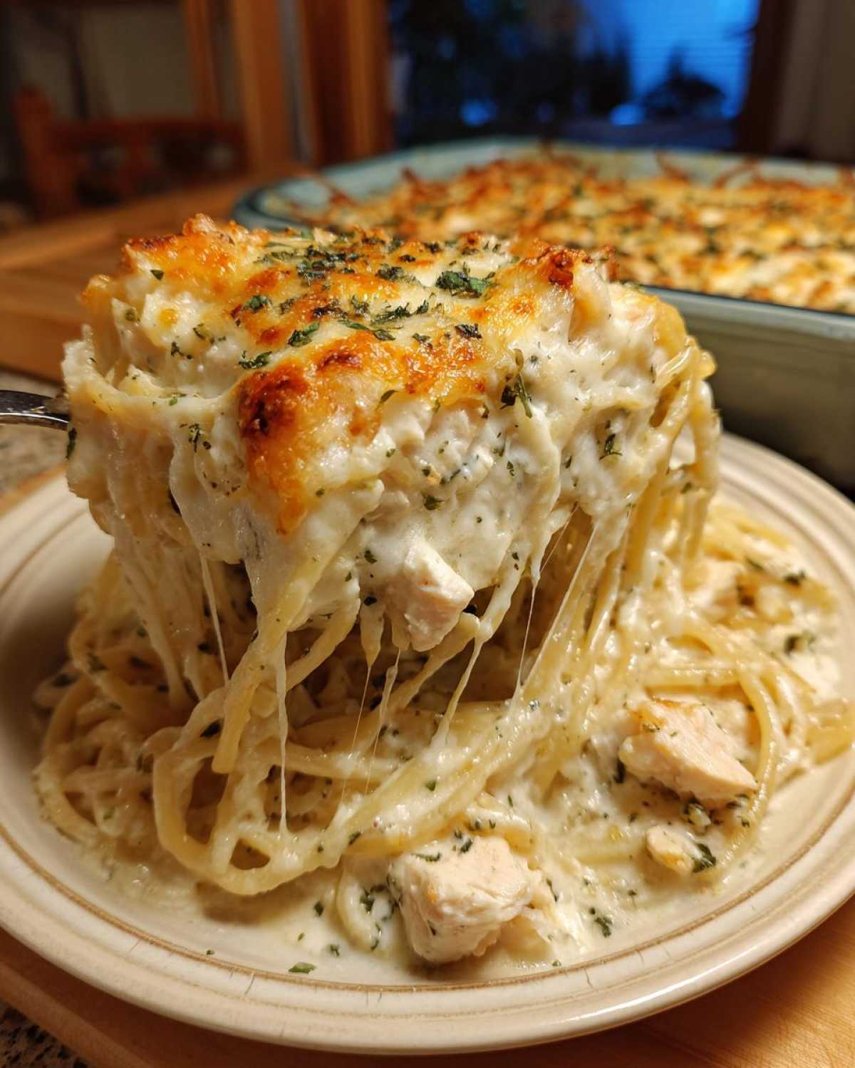 A serving of Cheesy Chicken Alfredo Bake with Mozzarella showing extreme cheese pull and golden brown topping.
