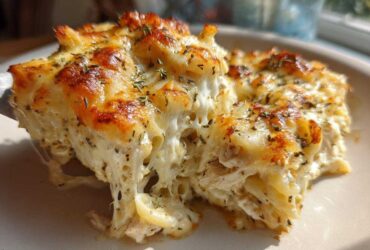 A serving of Cheesy Chicken Alfredo Bake with Mozzarella showing a dramatic cheese pull and golden-brown top.