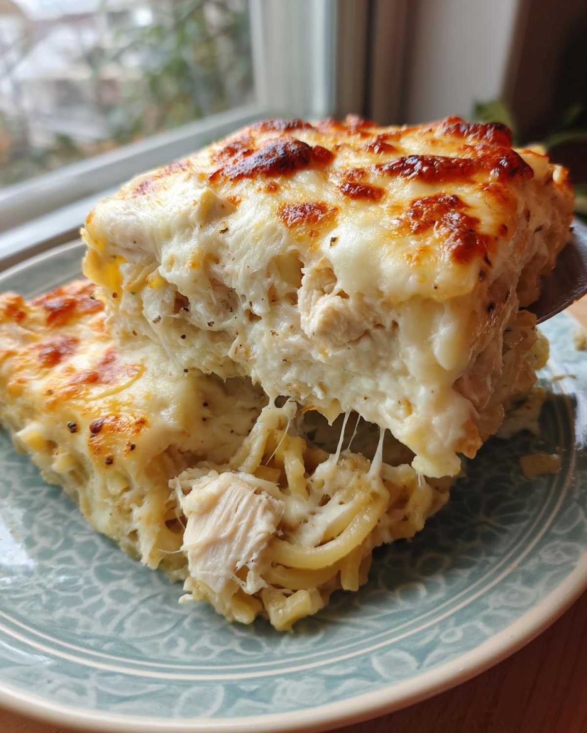 A serving of Cheesy Chicken Alfredo Bake with Mozzarella showing melted, browned cheese and stringy Alfredo sauce.