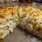 A cross-section slice of Cheesy Chicken Alfredo Bake showing tender chicken chunks mixed with pasta in a creamy sauce, topped with melted, bubbly cheese.
