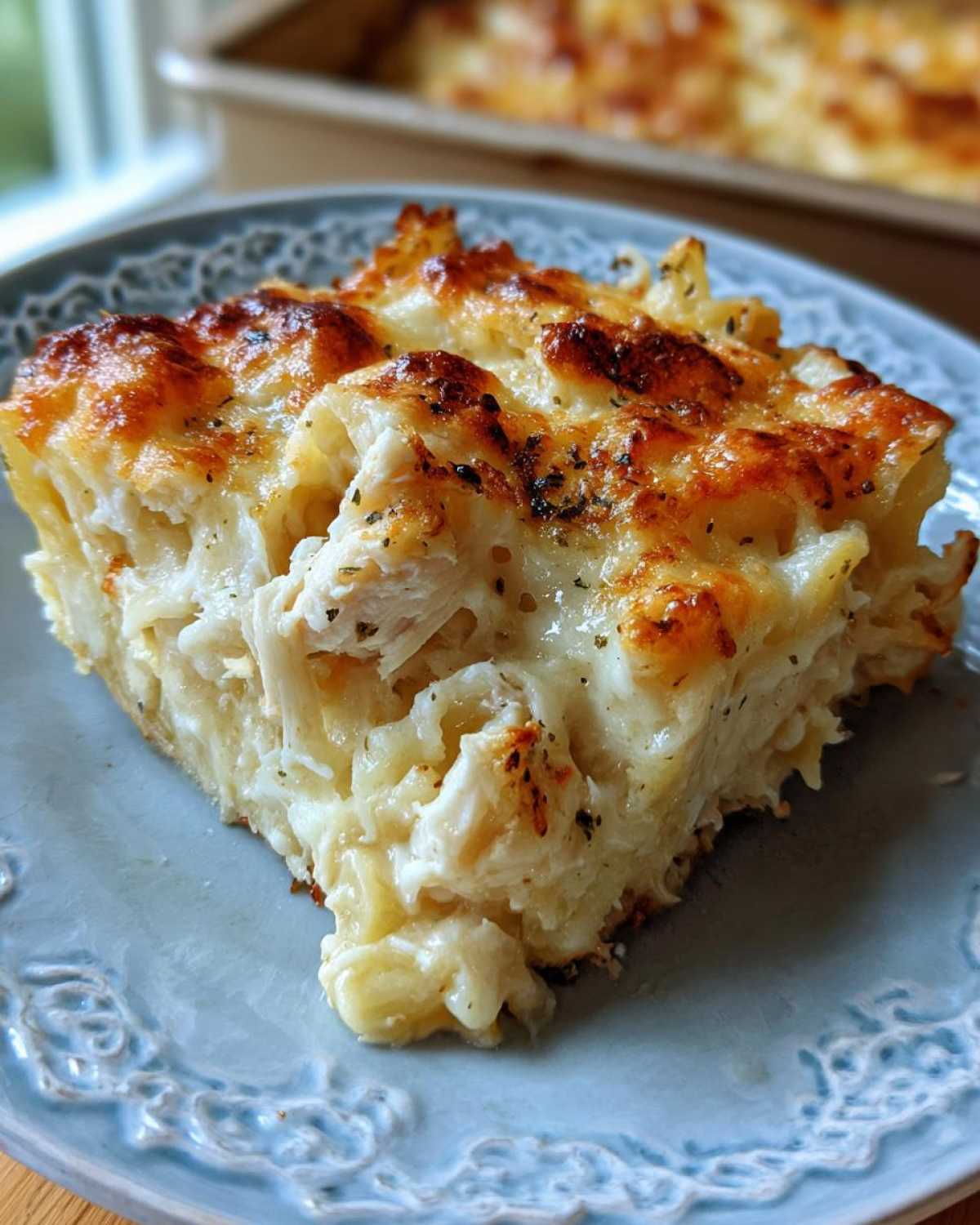 A generous slice of Cheesy Chicken Alfredo Bake with Mozzarella, featuring shredded chicken and pasta under a golden, bubbly cheese crust.