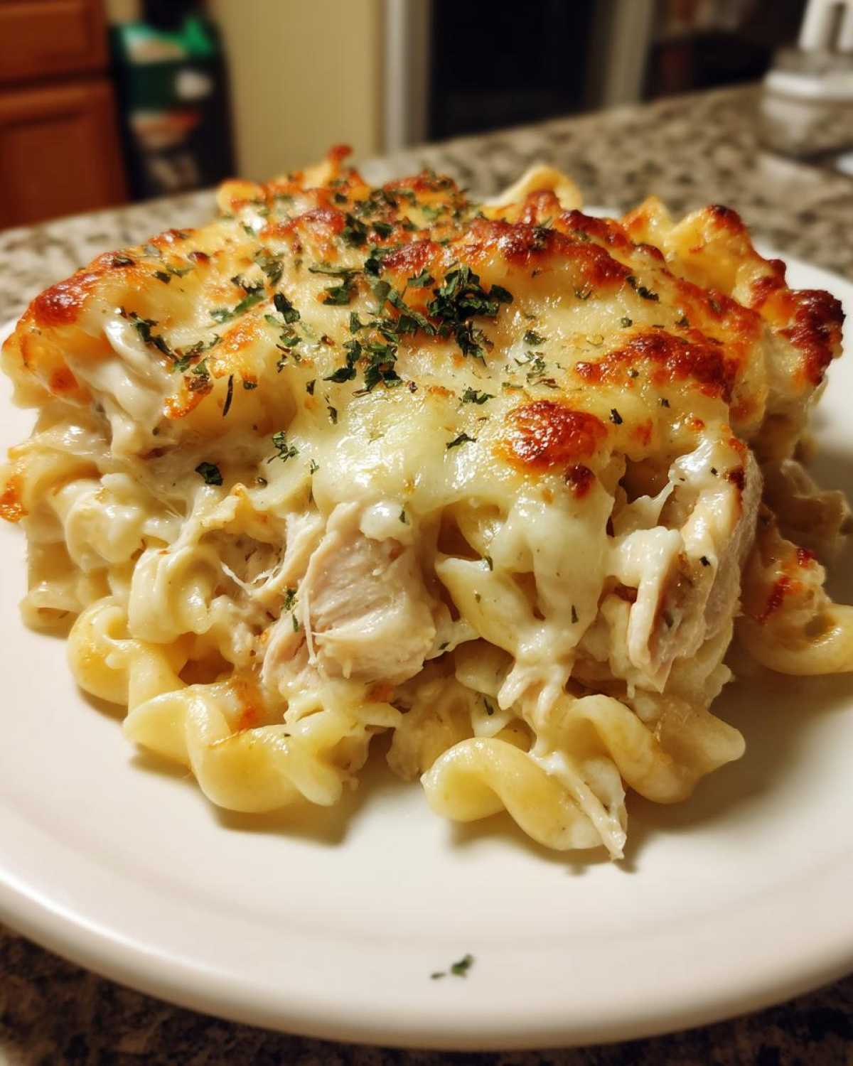 A close-up of a serving of Cheesy Chicken Alfredo Pasta Bake with Mozzarella, topped with melted, browned cheese and parsley.