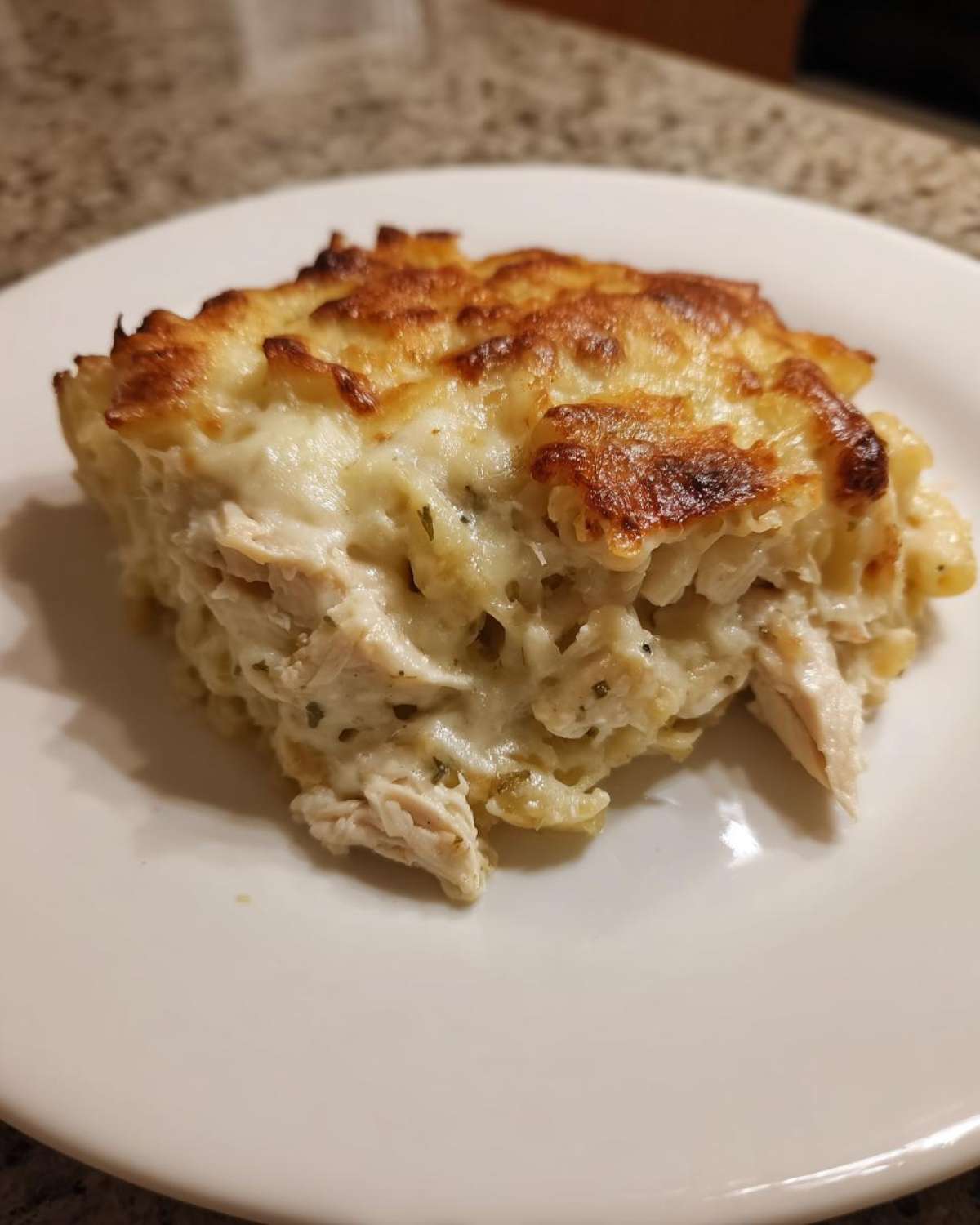 A close-up of a serving of Cheesy Chicken Alfredo Pasta Bake with Mozzarella, featuring a golden-brown, bubbly cheese crust.