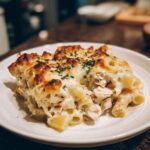 A close-up serving of Cheesy Chicken Alfredo Pasta Bake with Mozzarella, featuring baked, bubbly cheese and chopped parsley.