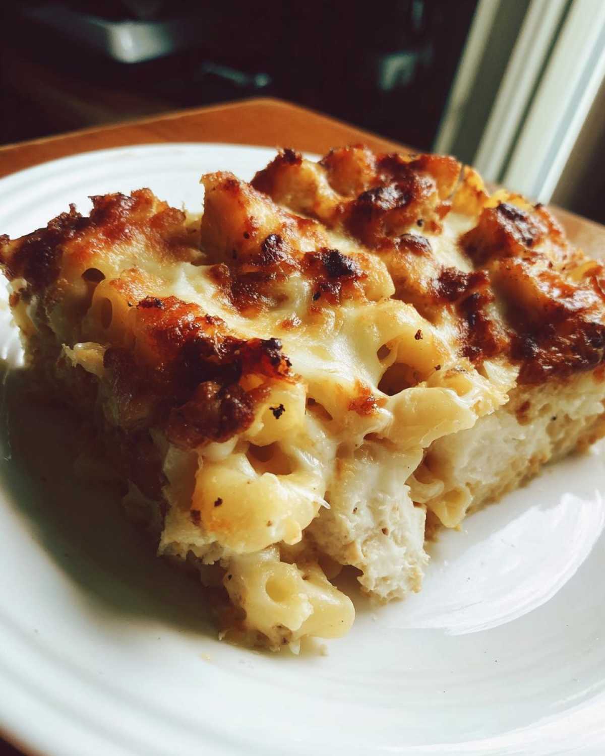 A close-up slice of Cheesy Chicken Alfredo Pasta Bake with Mozzarella showing baked, browned cheese topping and chunks of chicken.