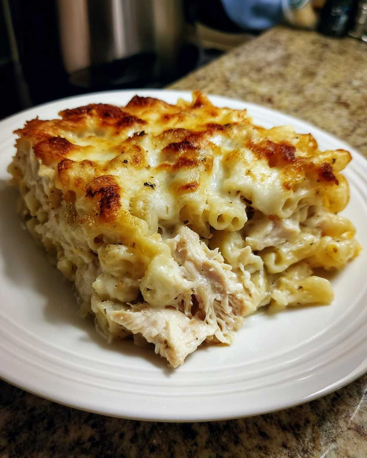 A generous serving of Cheesy Chicken Alfredo Pasta Bake with Mozzarella, featuring baked, browned cheese on top.