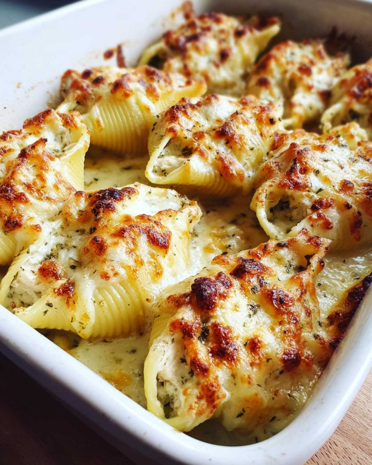 Close-up of baked Cheesy Chicken Alfredo Stuffed Pasta Shells in a white dish, topped with melted, browned cheese.