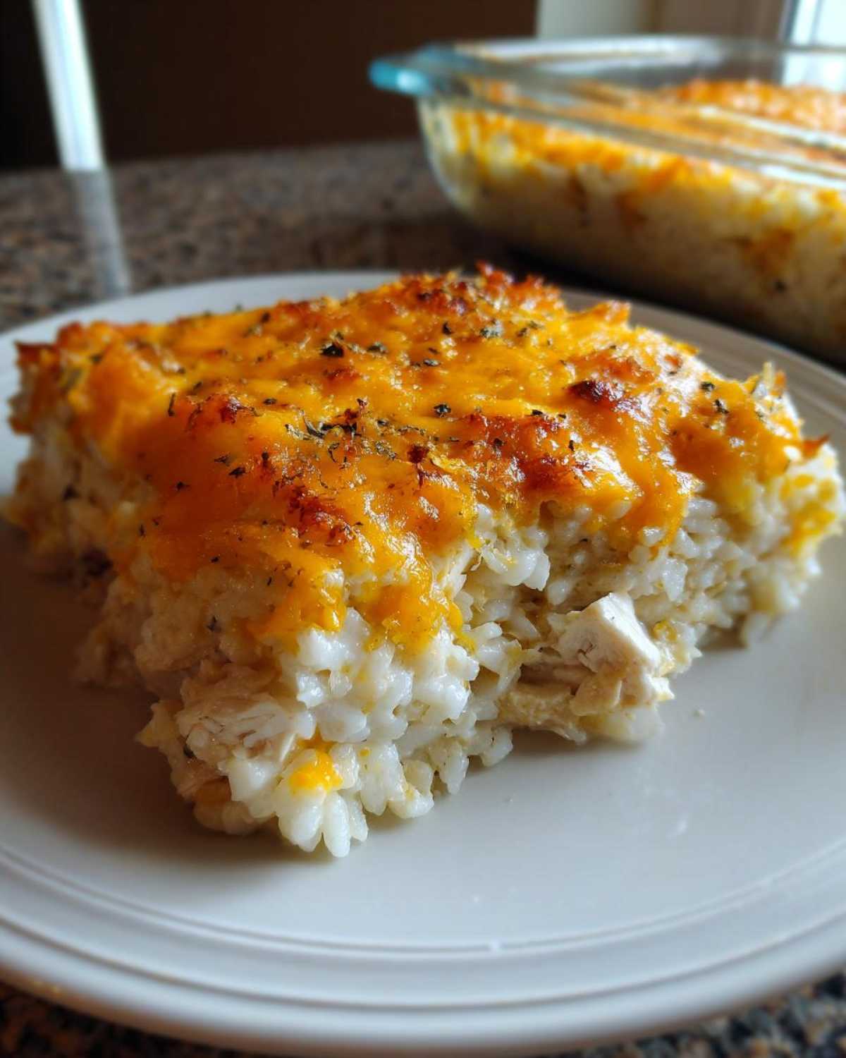 A generous serving of Cheesy Chicken and Rice Bake with Golden Top on a white plate, showing melted cheese.