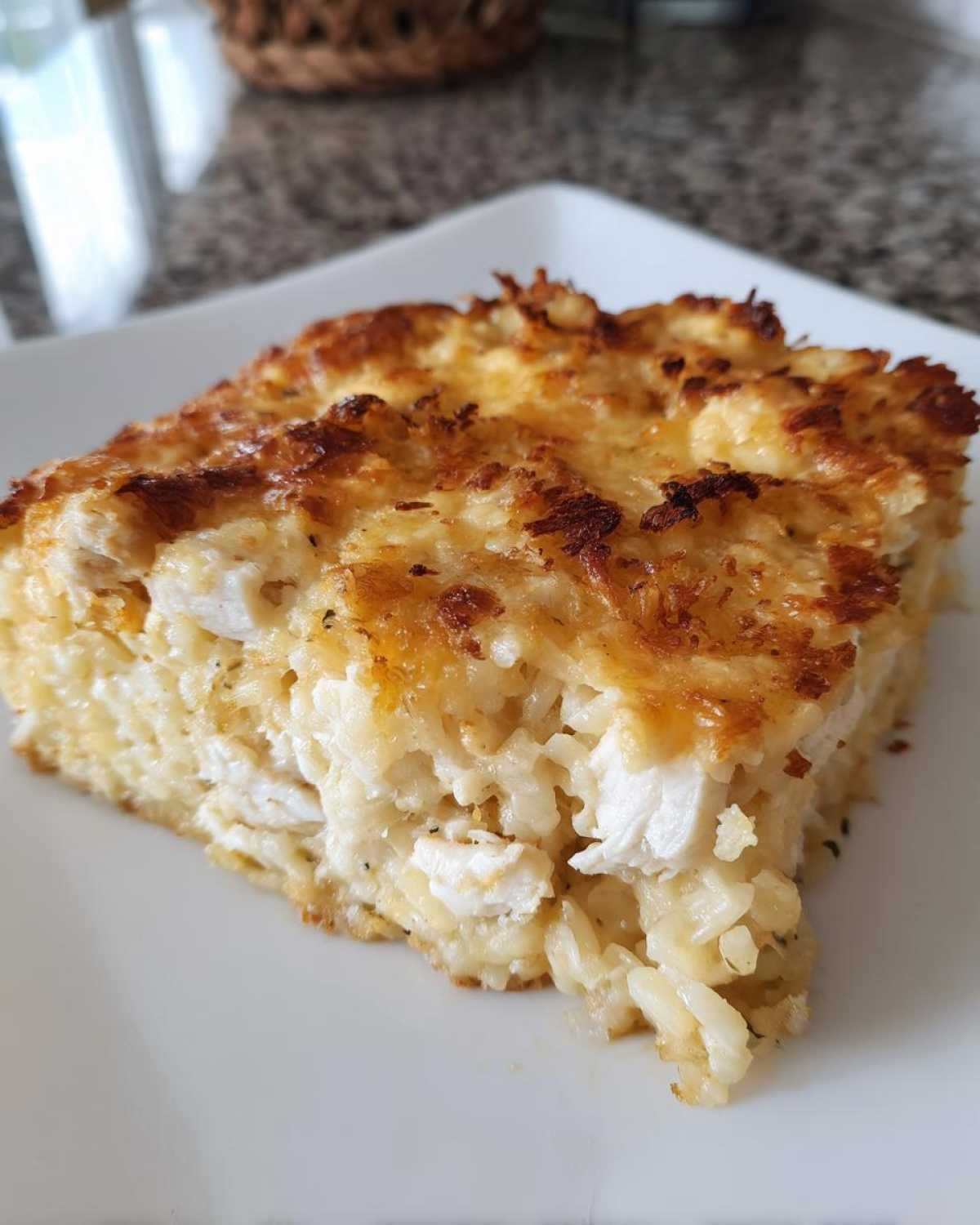 A close-up of a square serving of Cheesy Chicken and Rice Bake with a deeply golden, crispy cheese topping.