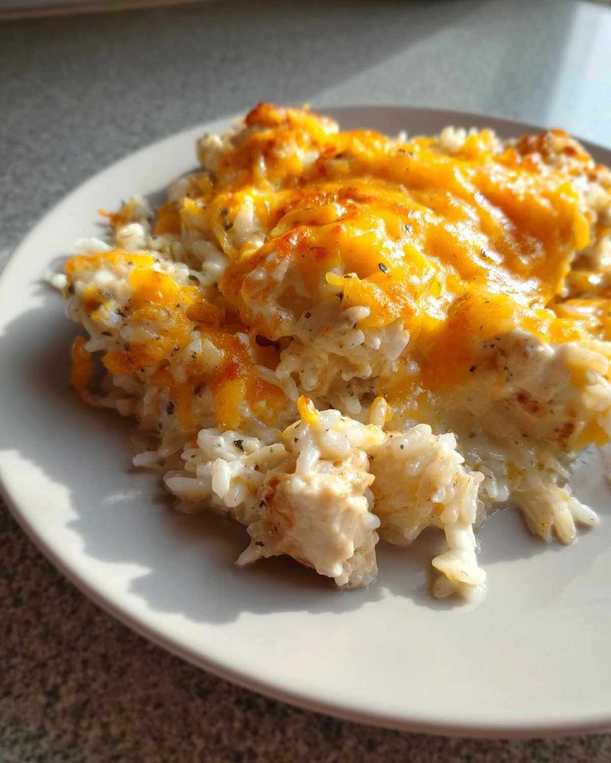 A close-up serving of Cheesy Chicken and Rice Skillet with Cream Sauce, topped with melted orange cheddar cheese.