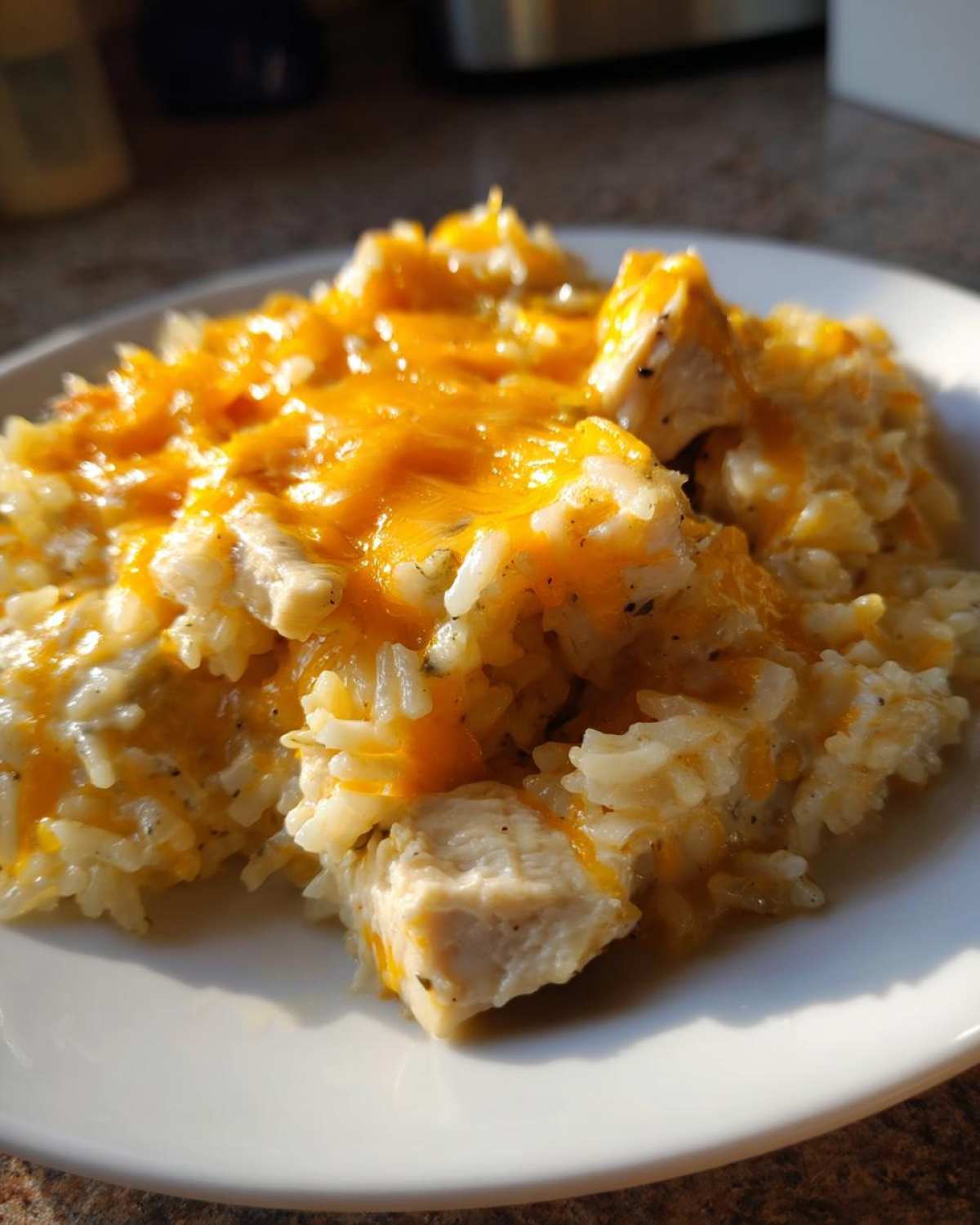 A close-up serving of Cheesy Chicken and Rice Skillet with Cream Sauce topped with melted cheddar cheese on a white plate.