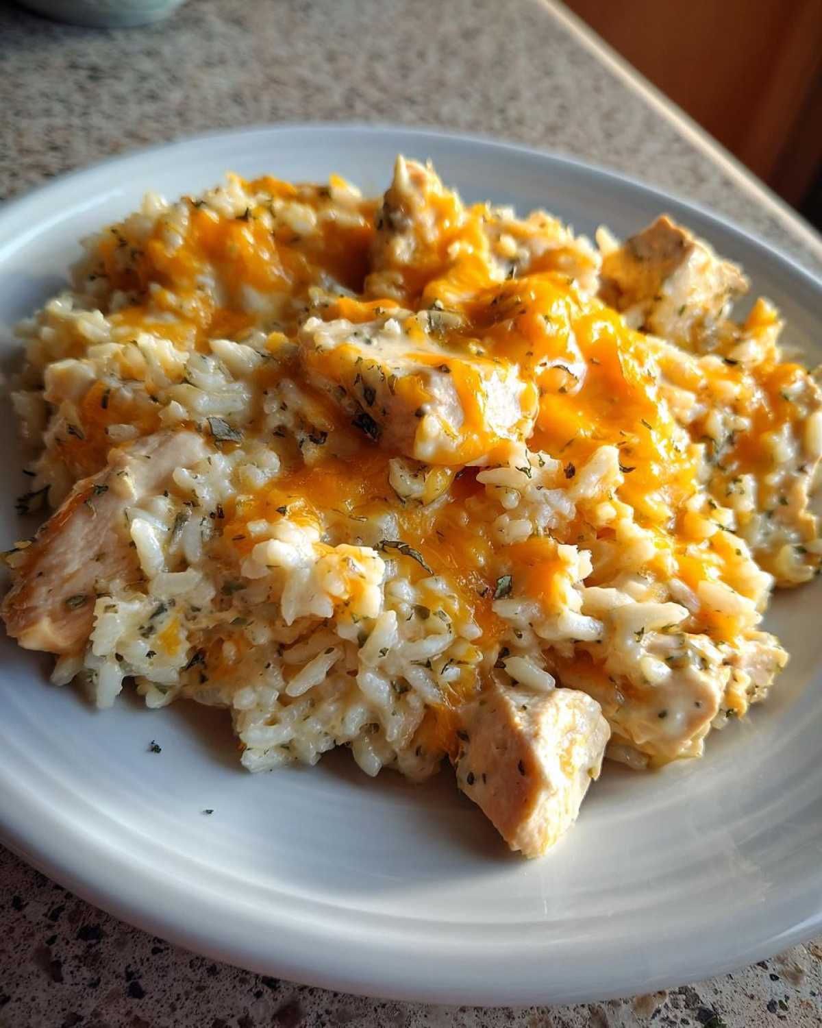 Close-up of Cheesy Chicken and Rice Skillet with Cream Sauce served on a white plate, topped with melted orange cheddar cheese.