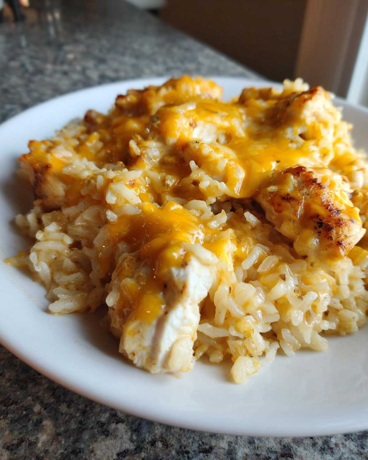 A close-up serving of Cheesy Chicken and Rice Skillet with Cream Sauce topped with melted cheddar cheese.