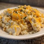 Close-up of a serving of Cheesy Chicken and Rice Skillet with melted cheddar cheese and parsley garnish.