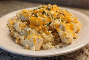 Close-up of a serving of Cheesy Chicken and Rice Skillet with melted cheddar cheese and parsley garnish.