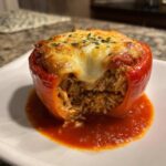 A close-up of a single Cheesy Chicken and Rice Stuffed Pepper topped with melted cheese and herbs, sitting in tomato sauce.