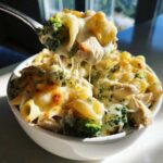 A spoonful of Cheesy Chicken and Broccoli Pasta Bake showing melted cheese stretching between the spoon and the bowl.